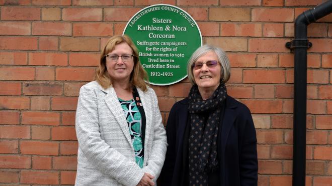 two women in front of green plaque