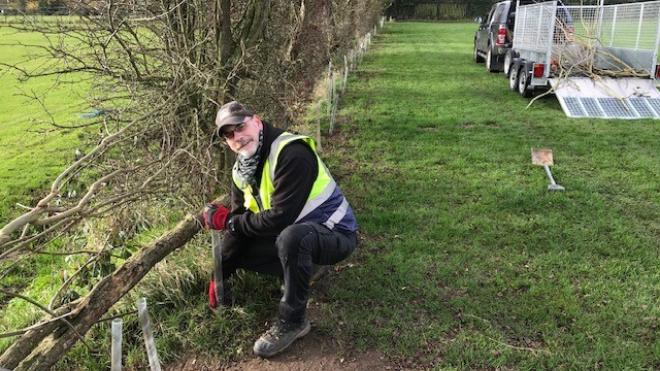 Burbage Parish Council Estates Officer Andy Harrison co-ordinated the planting of new native hedging plants which were part-funded by a County Council SHIRE Grant. Man wearing high vis knelt down planting trees in a line