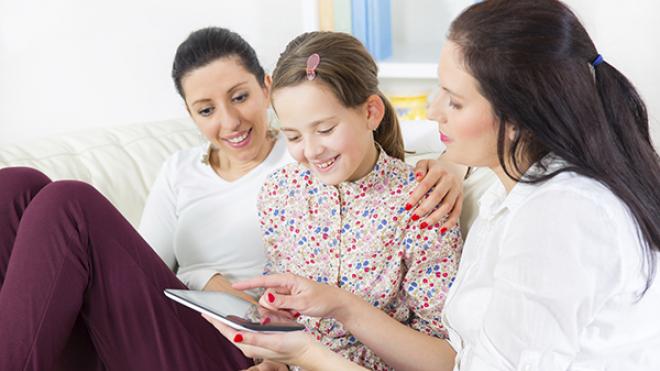 two ladies who are foster carers, and the girl they are fostering, are all looking and smiling at a tablet device