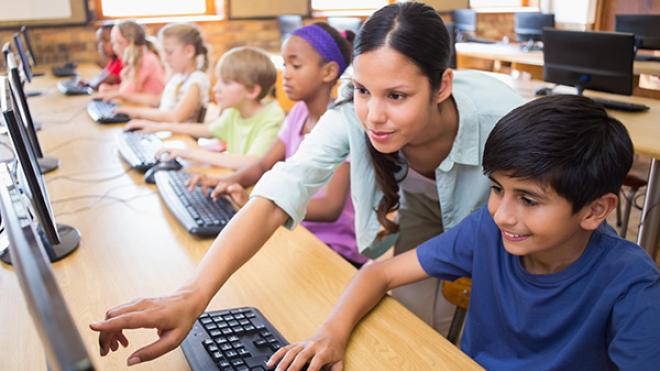 teacher helping a child use a computer in a classroom