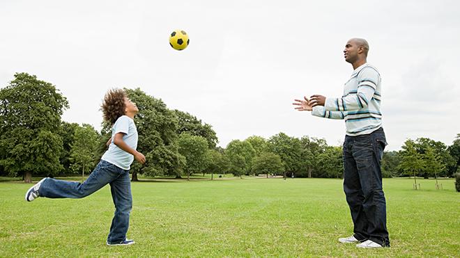 Child and adult playing football in a park