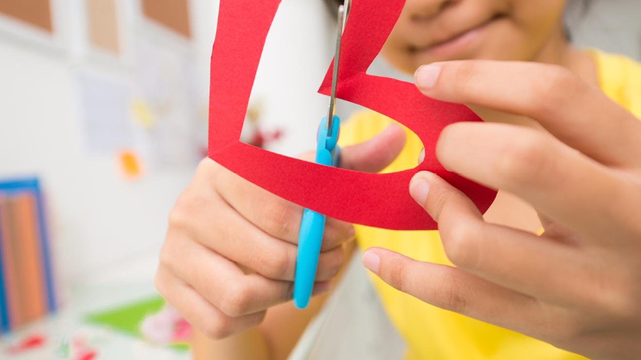 Child cutting out a red paper heart