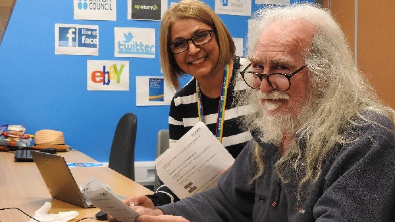 Teacher and student smiling and holding instruction papers in front of computer