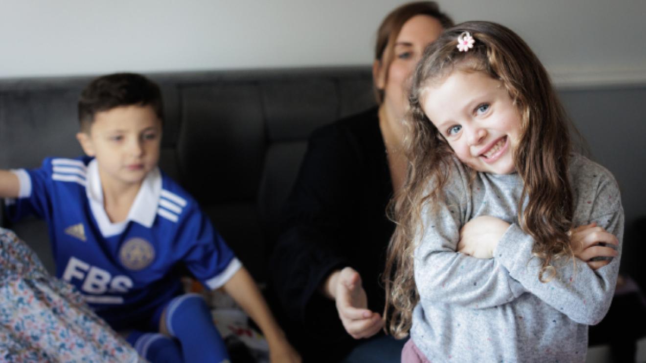 Young girl smiles at the camera with family members behind her