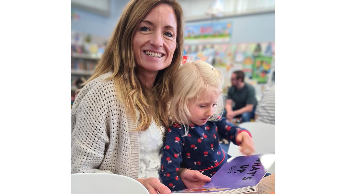Wriggly Readers at Leics Libraries Mother sitting with her child on her knee. The child is reading from a children's book