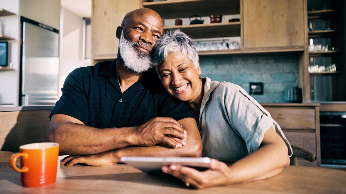 Couple sitting at a kitchen table looking at a tablet and smiling