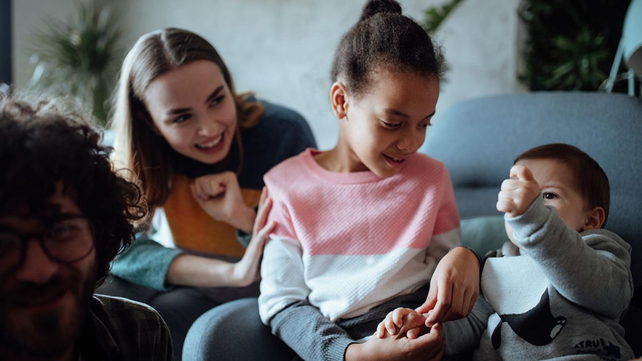 child looking at younger baby holding their hand whilst carer looks on behind her