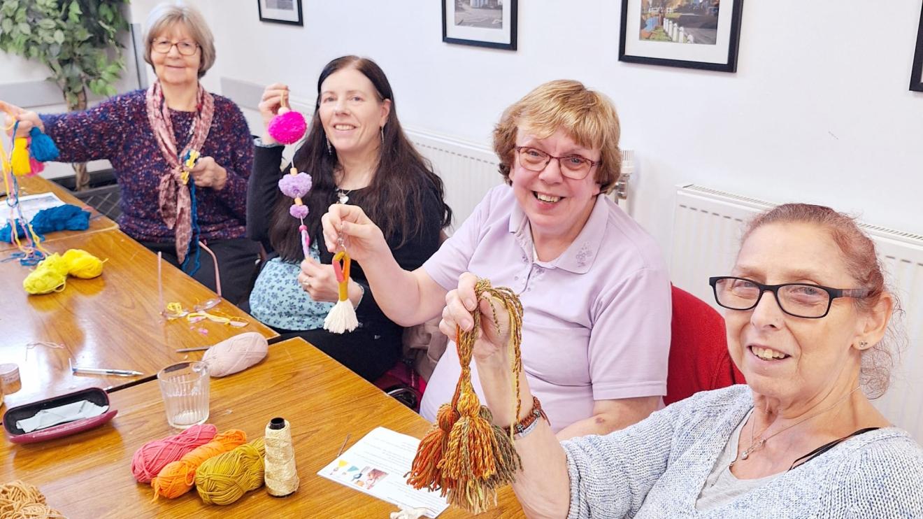 four people sat at a table smiling holding up their craft items
