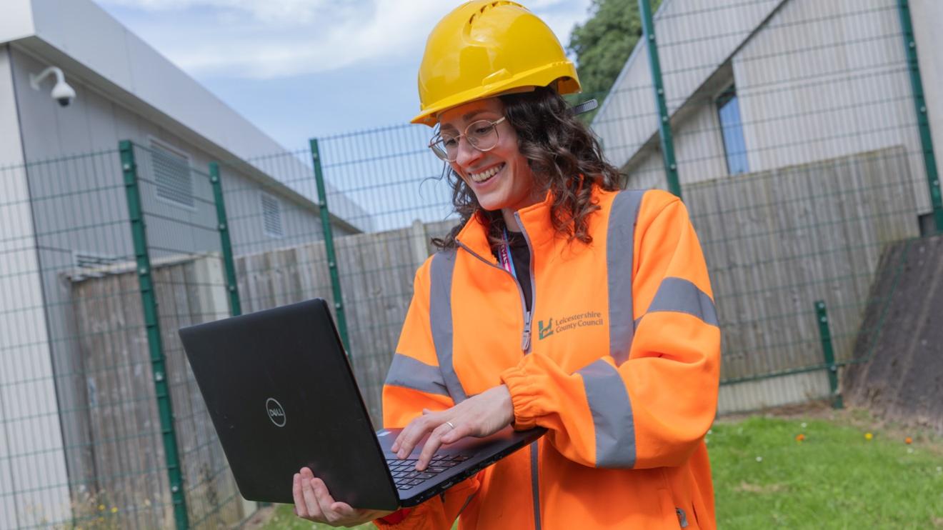 Environment and Transport staff wearing a hi vis jacket and hard hat, holding a laptop