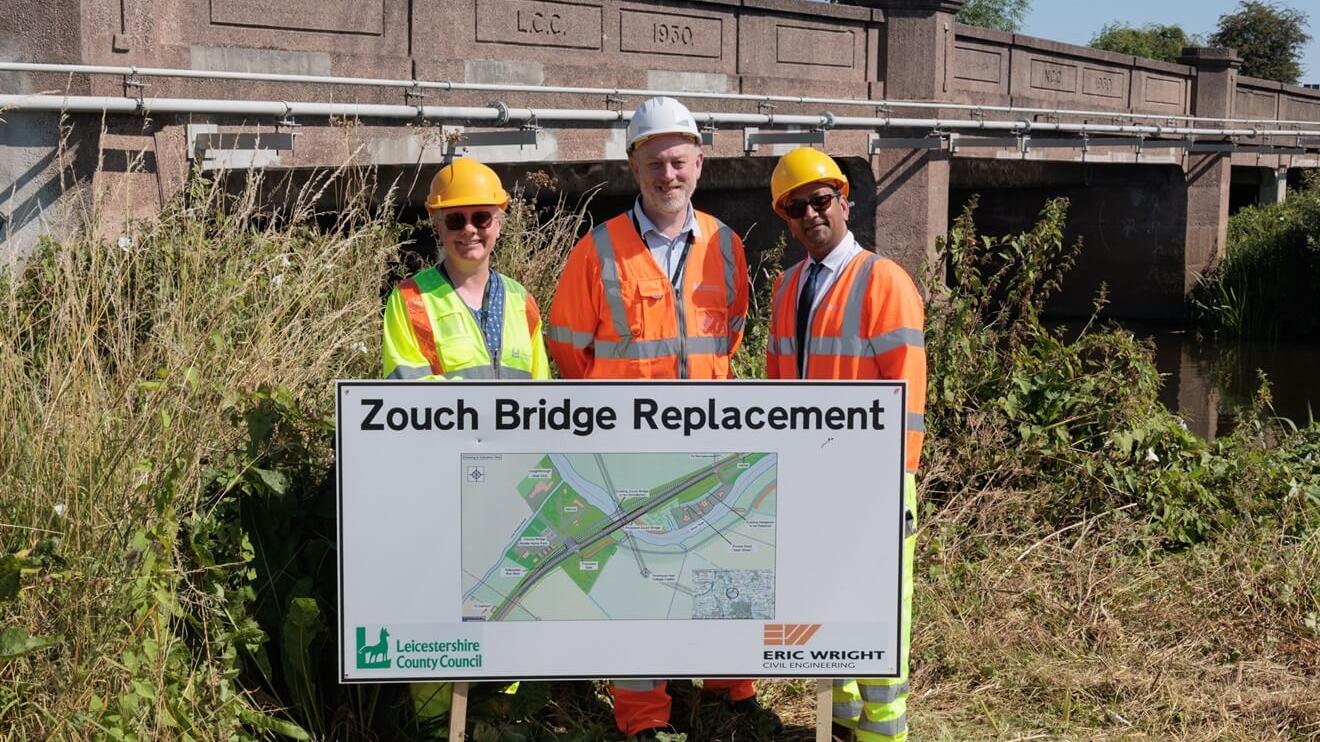 Highways staff wearing hard hats and hi-vis jackets, standing between the current Zouch Bridge and scheme's sign.