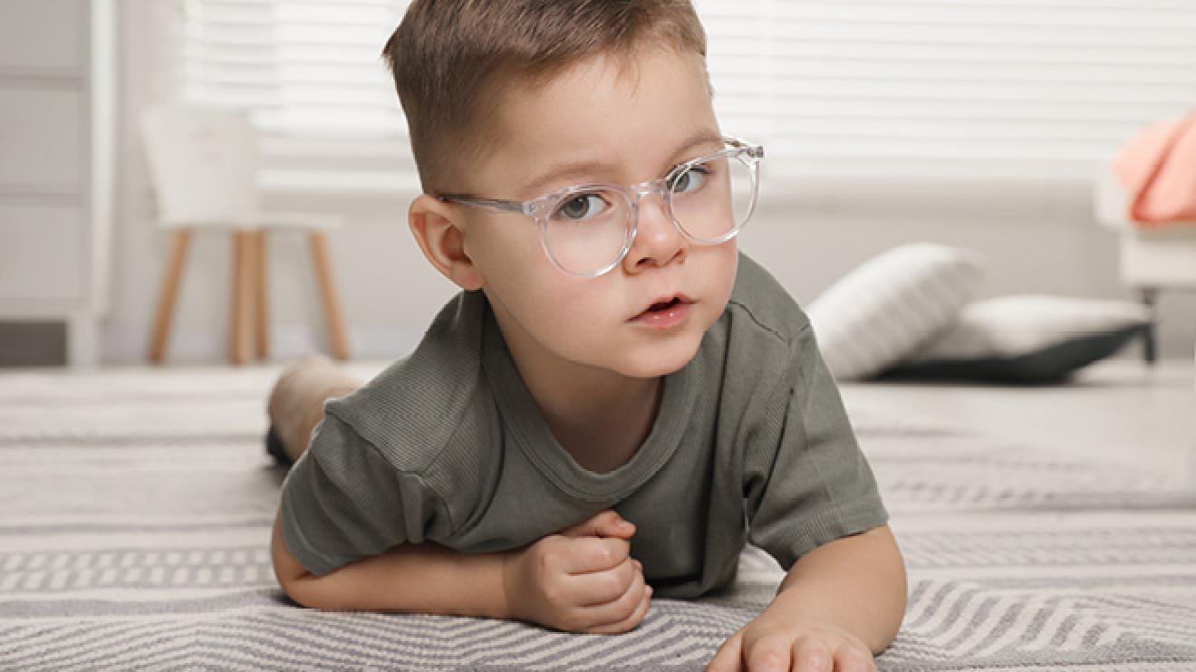 A little boy with glasses playing on the floor in a bright, clean room