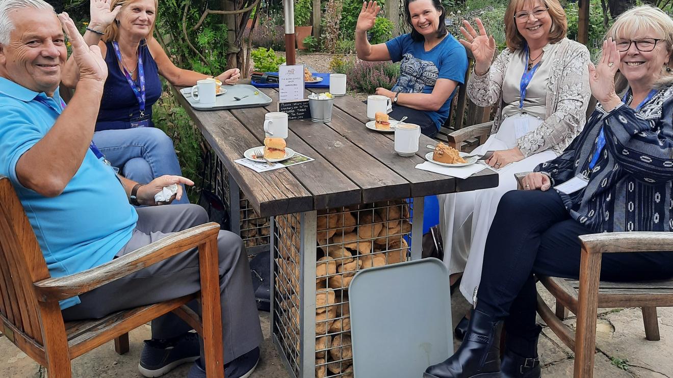 A group of carers sitting at an outside wooden table waving at the camera