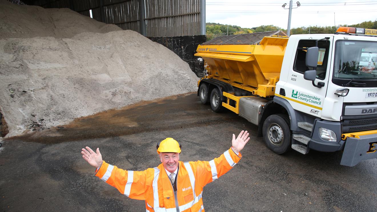 Cllr Trevor Pendleton in hi-vis and helmet in front of a gritting lorry and a big pile of gritting salt