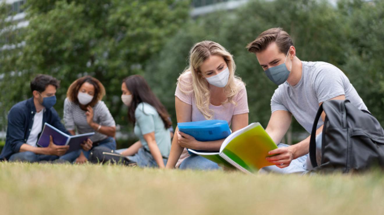 Young people sitting in a field wearing face masks