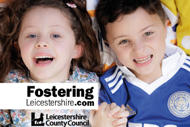 Two young children holding hands. A girl with brown wavy hair and a boy wearing a Leicester City top 