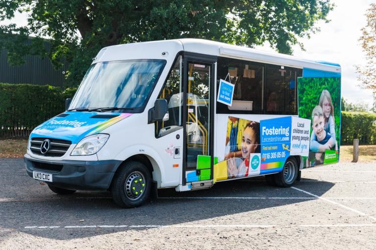 A white minibus with colourful livery promoting fostering 