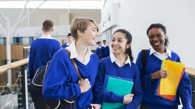 Three children in a school corridor wearing blue jumpers and smiling 
