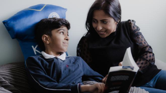 Young boy and carer smile at each other whilst reading