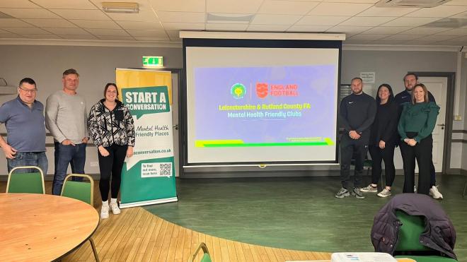 Representatives of the FA, County Council and football clubs standing by a projector screen at a mental health friendly clubs training session