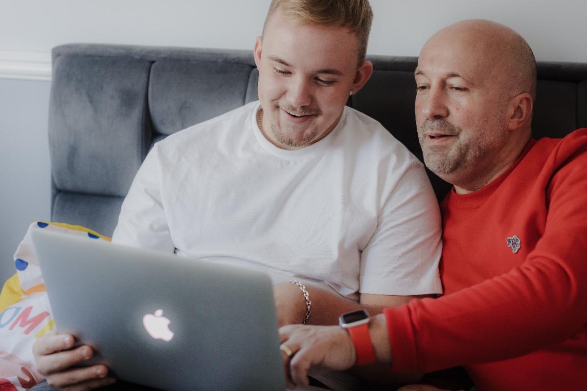 Foster carer and a young boy sitting on a sofa and looking at a laptop