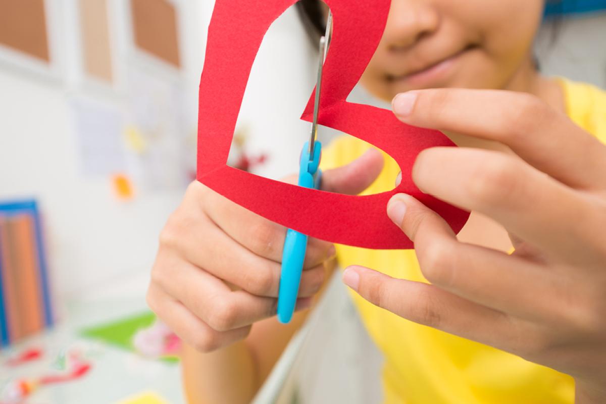 Child cutting out a red paper heart