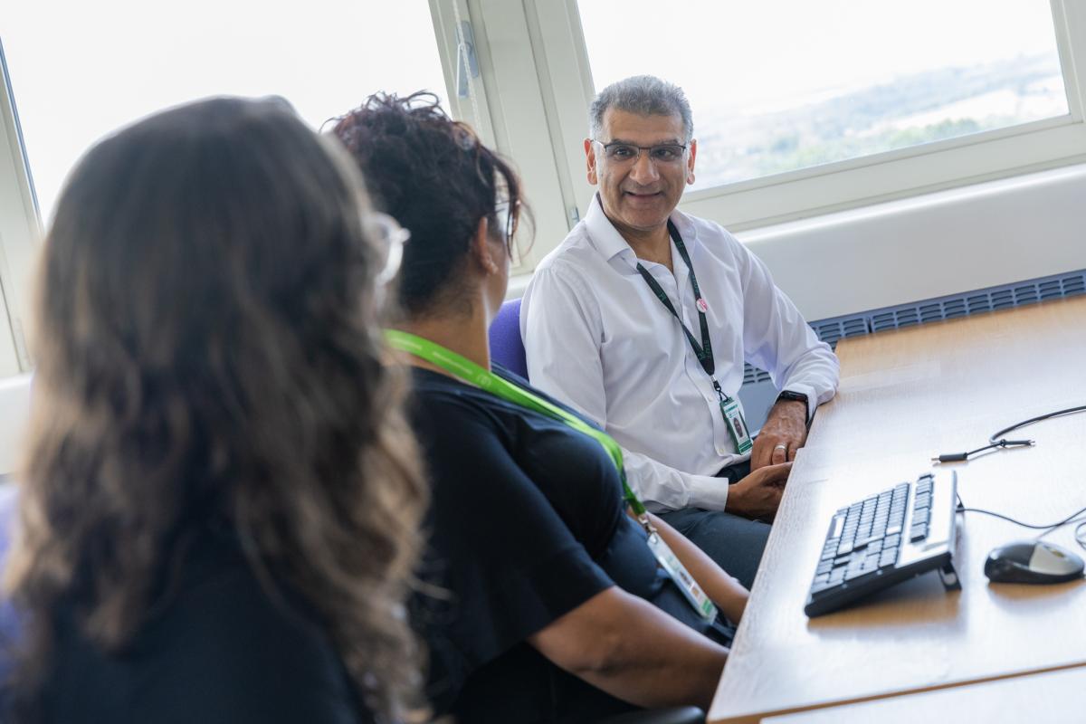 Three Leicestershire County Council staff sitting in front of a desk facing each other and engaged in conversation