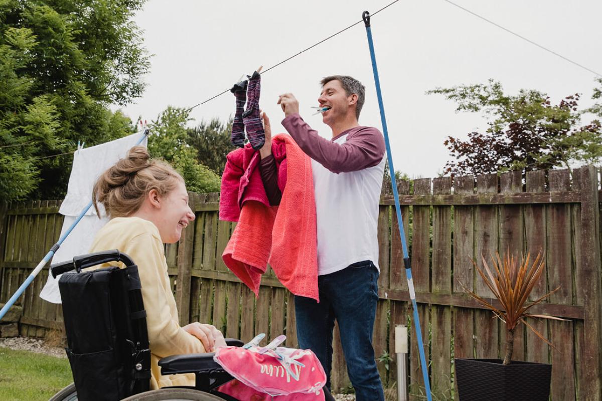 man hanging washing out with girl in wheelchair