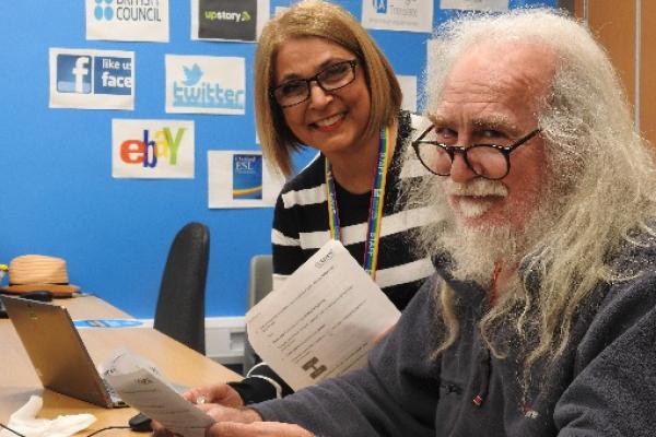 Teacher and student smiling and holding instruction papers in front of computer