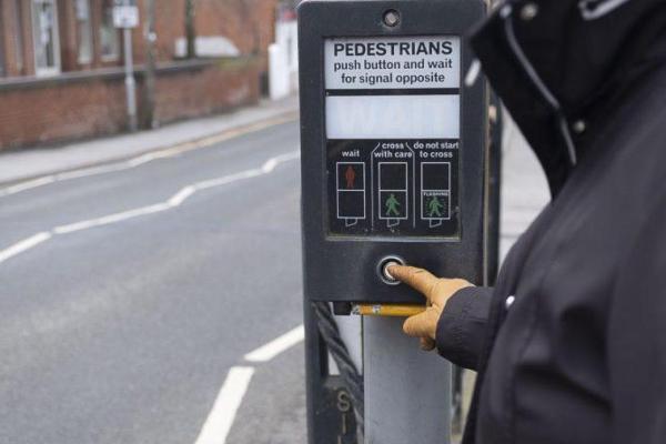 Person pressing the button on a pelican crossing.