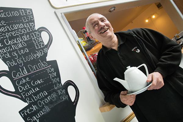 man holding a tea pot, standing in a coffee shop