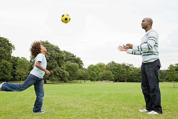 Child and adult playing football in a park